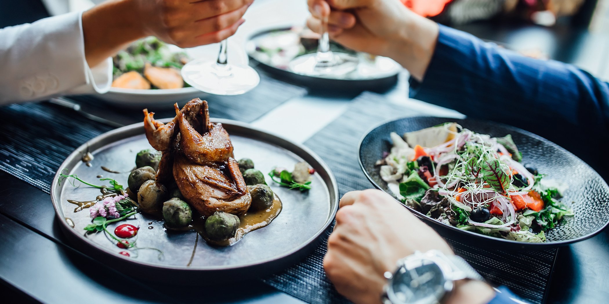 Succulent duck dishes served to diners with salad and wine on a contemporary black table