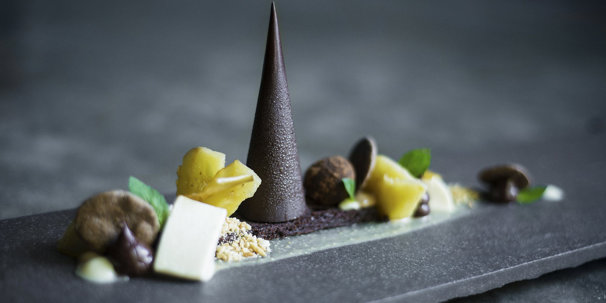 High-end beautifully prepared chocolate pyramid with lemon sorbet, mint and chocolate truffle served on a decorative slab of marble