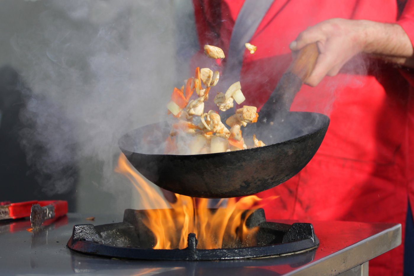 Outside cooking - a chef pan-fries chicken over a wok with flames and smoke