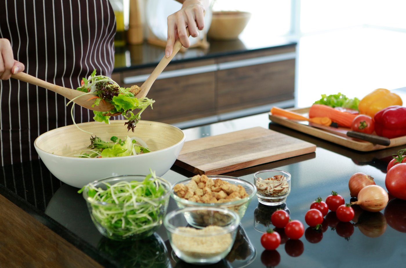Chef preparing a salad dish with cutting board and ingredients on a black graniwe worktop