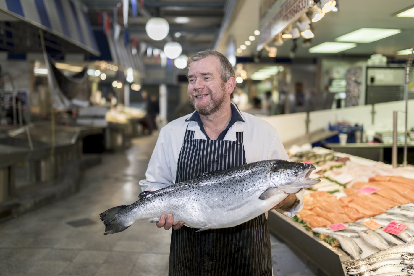 Fishmonger in a food court holding a large fresh fish