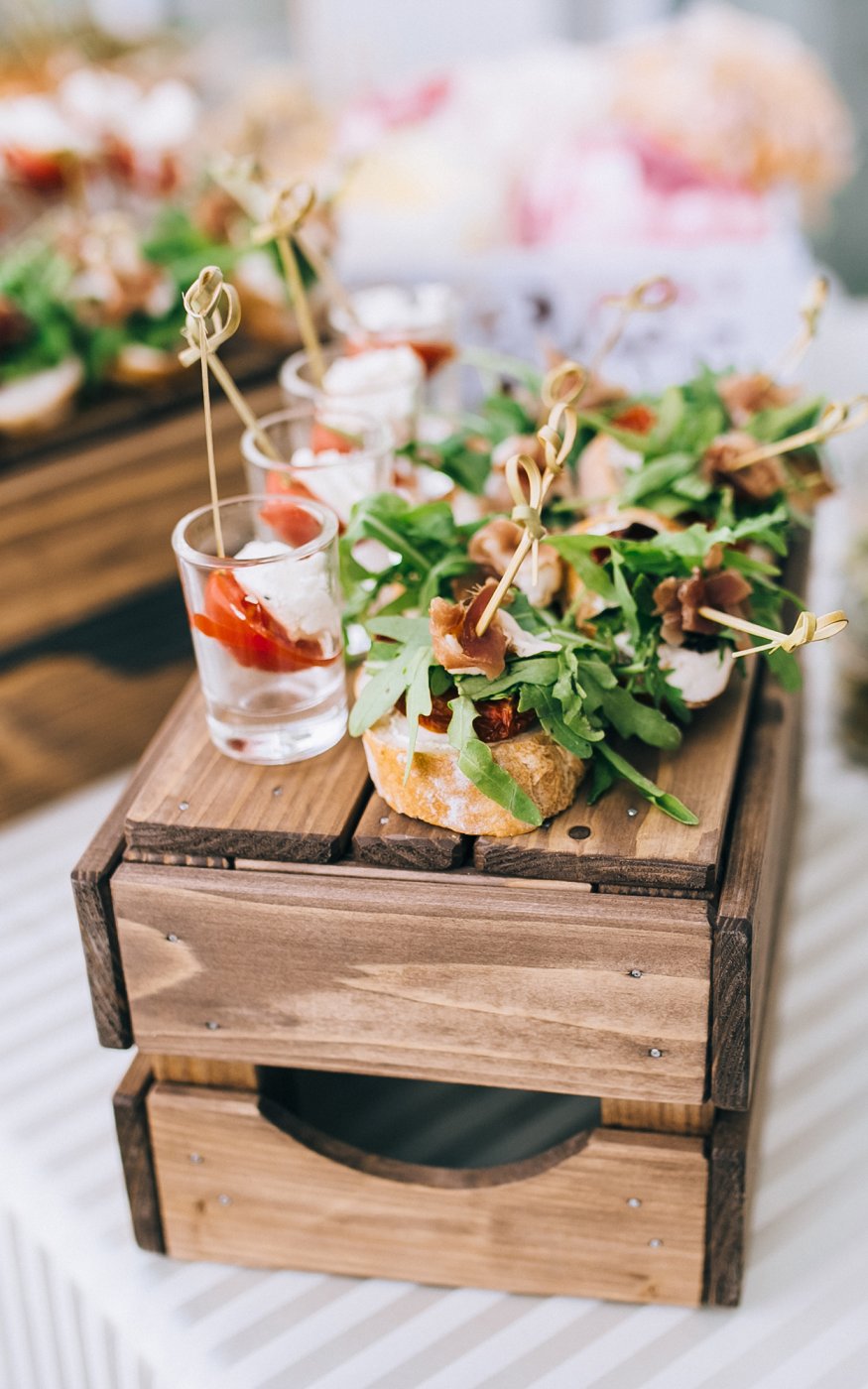 A rustic crate acting as a tray for a selection of gourmet finger food including rocket and chicken skewers