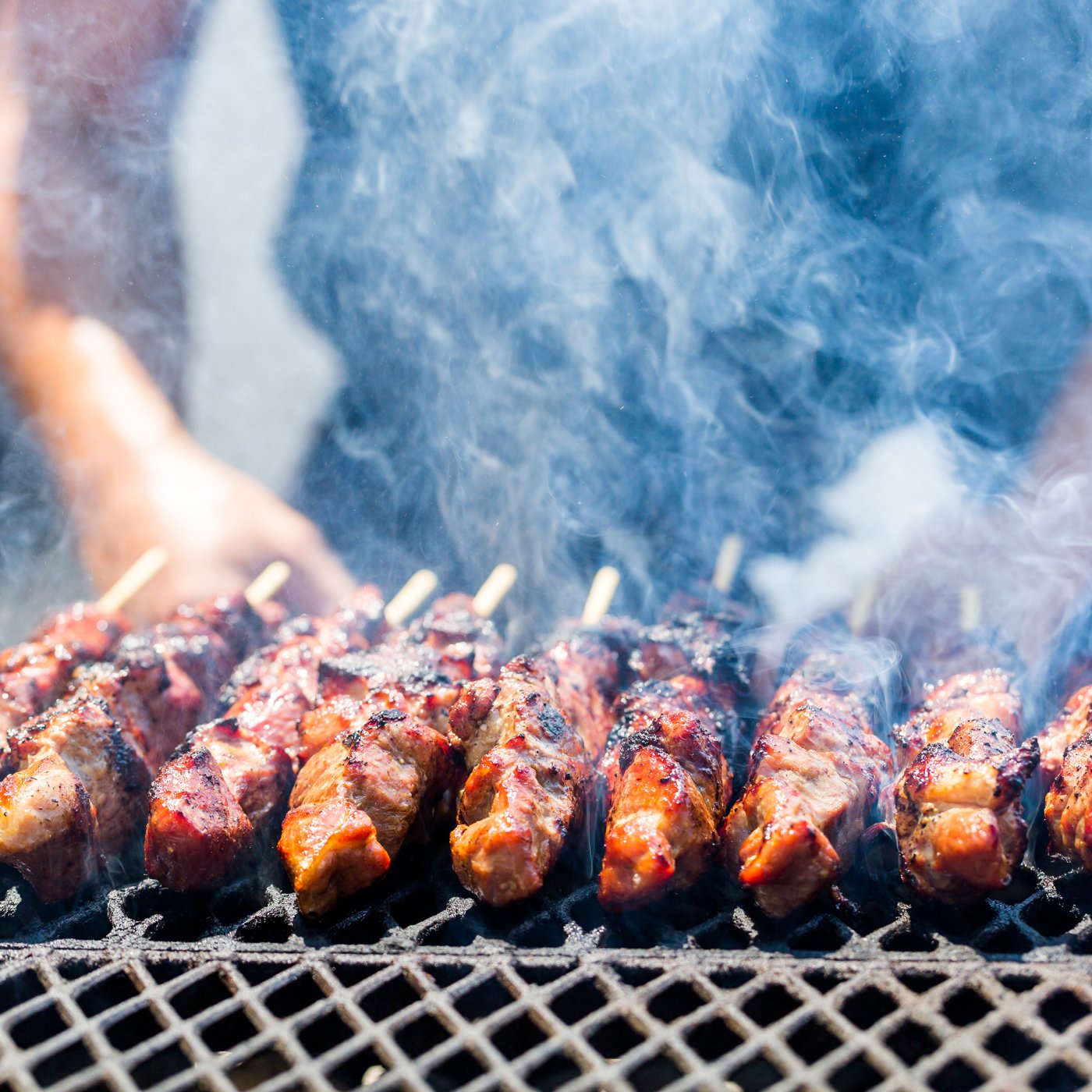 Lamb koftas sizzling in a row on an outdoor grill, with chef close-by