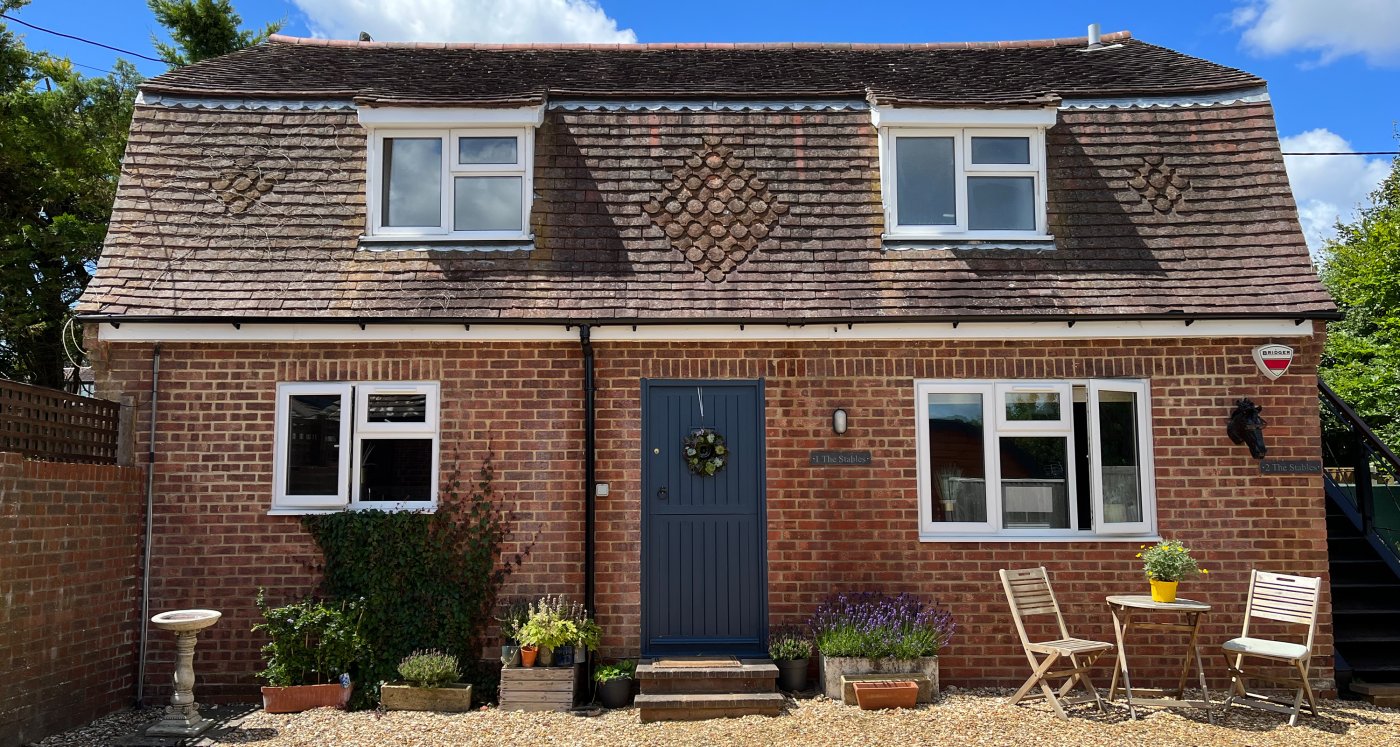 External view of the Stables Ground Floor, rustic building, grey door, stone drive